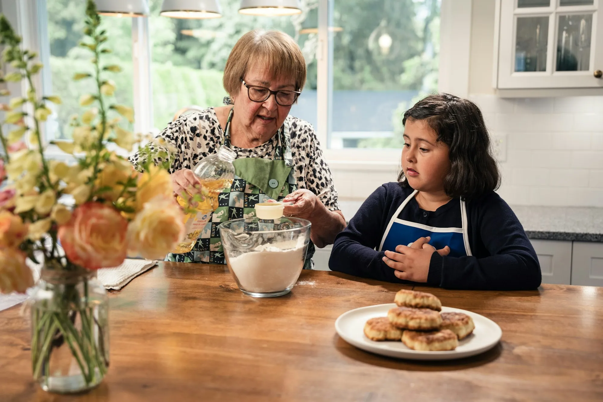 An older woman and a child cooking together in a sunlit kitchen