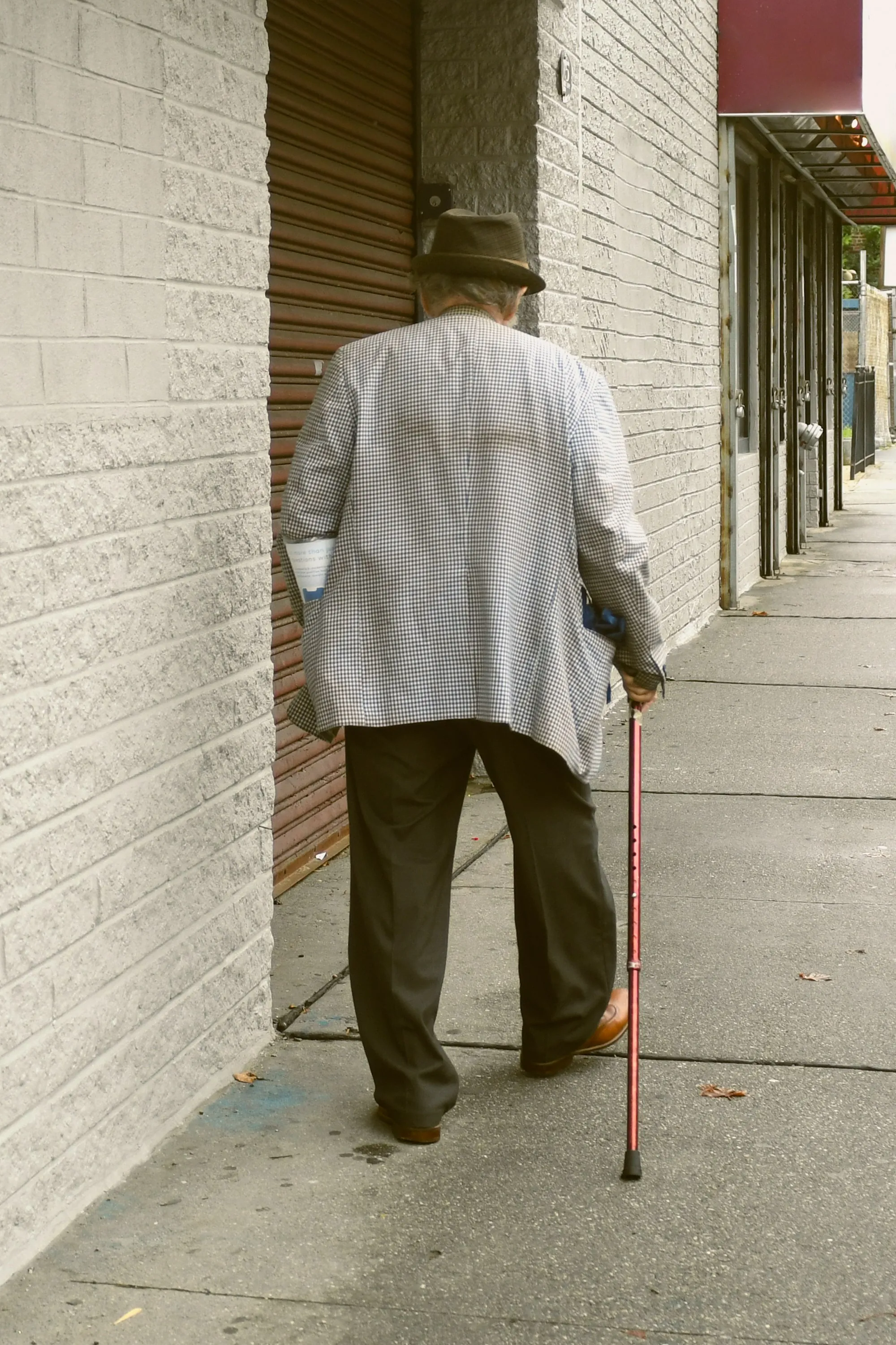 An older person walking with a cane on a paved path